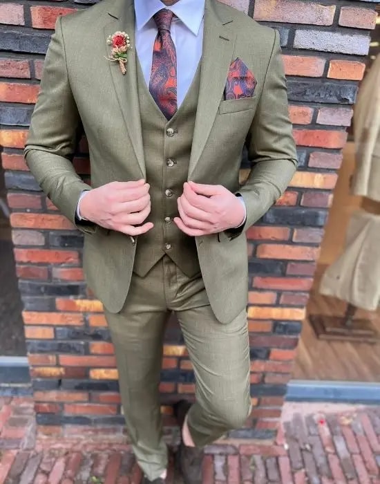 Homme en costume trois pièces vert olive devant un mur de briques